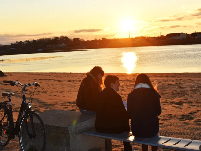 Trois personnes observant le couché de soleil depuis le port de Larros
