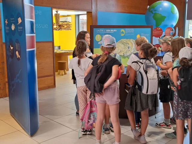 Groupe d'enfants écoutant attentivement l'une des guides de la maison de l'huitre.