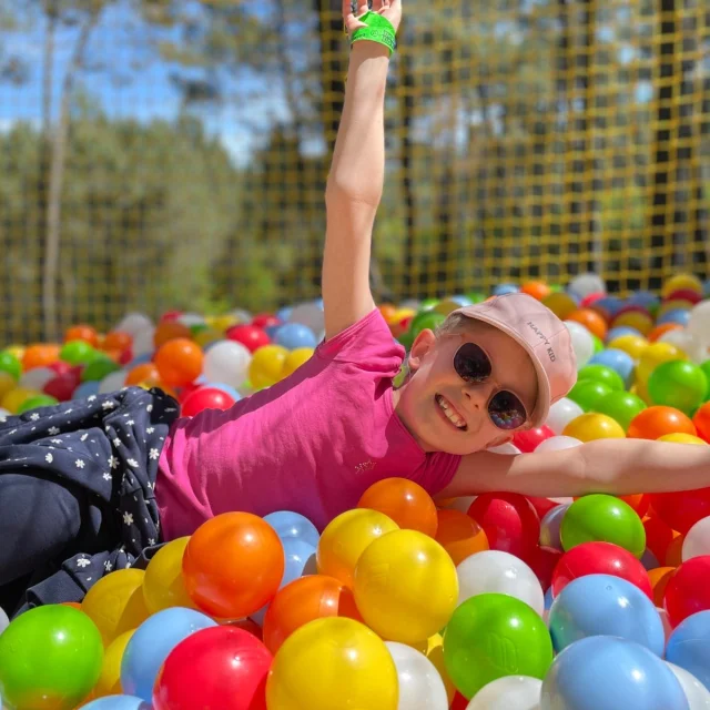 Enfant jouant dans une piscine de boules de couleurs, perché dans les arbres, faisant partie du parc de loisirs la cité perchée
