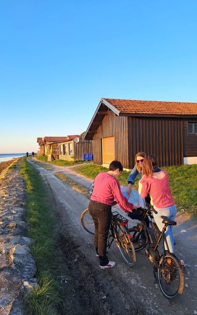 Des touristes à vélo sur le port de Larros qui sont en train de regarder la carte des déplacements pour connaître leur itinéraire