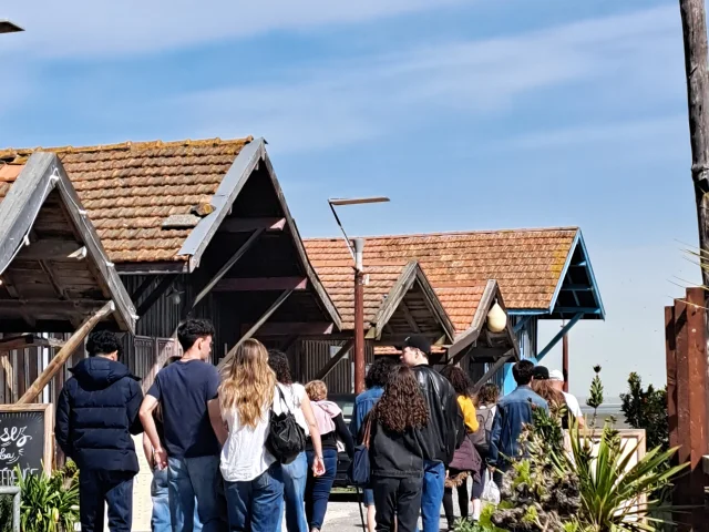 Groupe de personnes qui suit la visite du Port de Larros en passant devant les cabanes ostréicoles