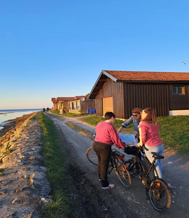 3 jeunes femmes à vélo sur le port de Larros en train de regarder le plan des pistes cyclables