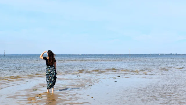 Jeune femme qui marche au bord de l'eau au port de Larros en regardant l'horizon